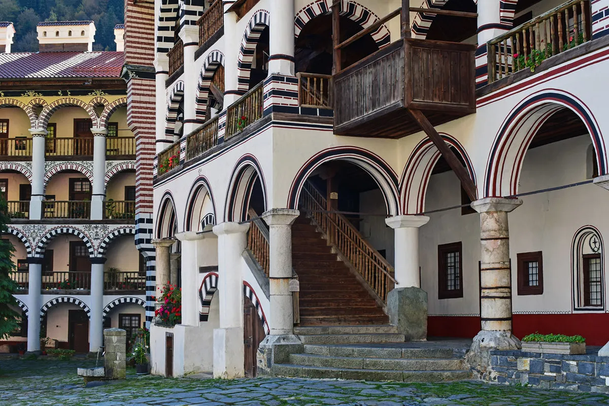 Visitors in the cobblestoned courtyard of a Bulgarian monastery with striped National Revival architecture