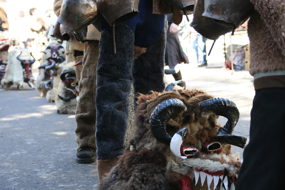 Costumed dancers in elaborate Kukeri masks and bells at a Bulgarian masquerade festival